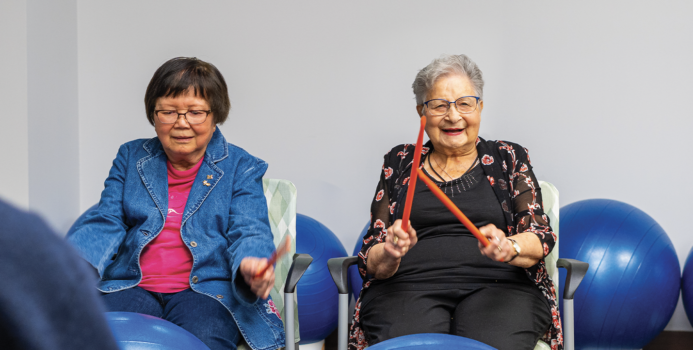 Two senior women - one caucasian, the other asian, are having fun taking part in a DrumFit class