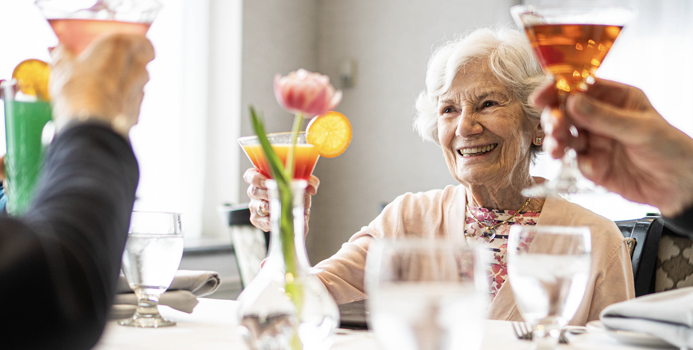 A senior woman raising her glass to cheers other seniors at a table